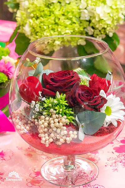 Compo de roses rouges et de fleurs blanches dans un vase en verre sur pied